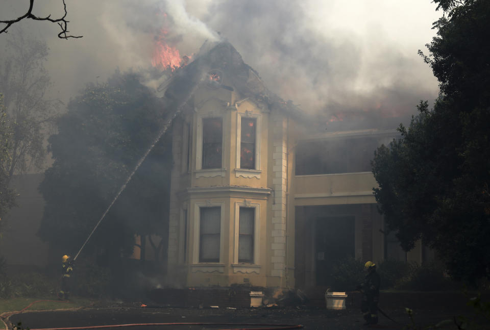 Firefighters douse a burning building at the University of Cape Town, South Africa, Sunday, April 18, 2021. A wildfire raging on the slopes of Table Mountain forced students to evacuate their residence as firefighters battled the blaze. (AP Photo/Nardus Engelbrecht)