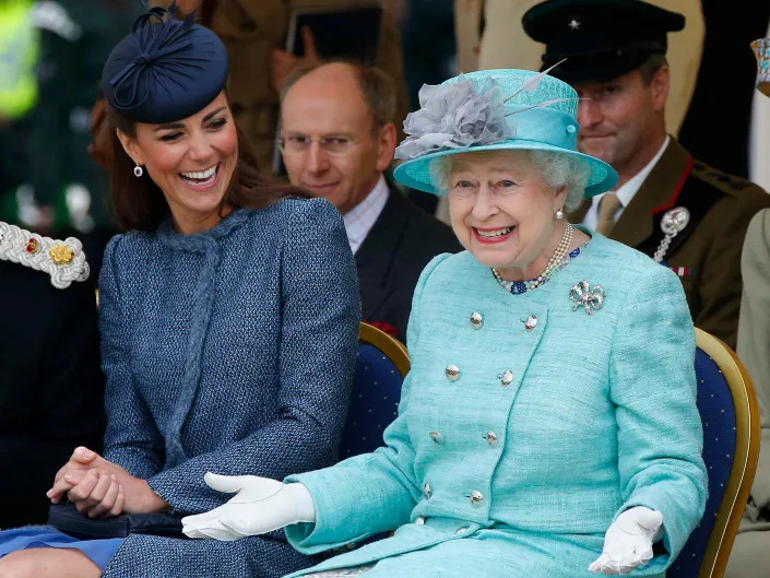Queen Elizabeth gestures while watching a children's sporting event as Kate Middleton looks at her and laughs