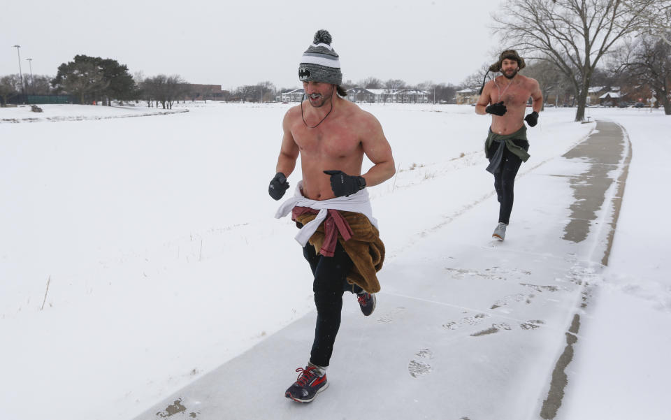 Same Reals, left, and Tyler Panko run shirtless through Wichita, Kan., Monday, Feb. 15, 2021. Reals said he tries to run a 5k on the coldest day of the year. The temperature during their run was -3, with a wind chill of -11. Frigid temperatures continue to grip with the middle of the continent. (Travis Heying/The Wichita Eagle via AP)