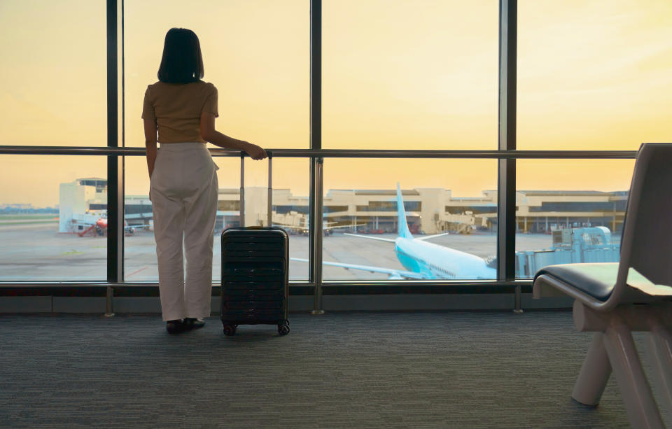 Frau steht bei Sonnenuntergang mit Koffer und beobachtet die Flugzeuge