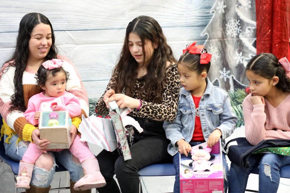 Isela Molina sonríe mientras su hija de 10 años Emily Ayala (centro) abre un regalo durante el evento de Navidad de la Familia Migrante 2023 que tuvo lugar en la biblioteca de la Firebaugh High School el 13 de diciembre.