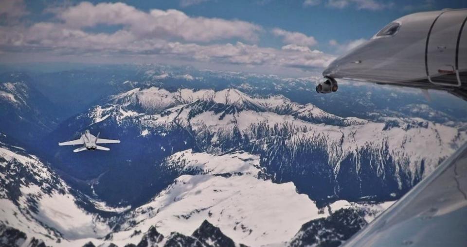 The Embraer Phenom 300E follows a fighter jet above a mountain range during filming of "Top Gun: Maverick."