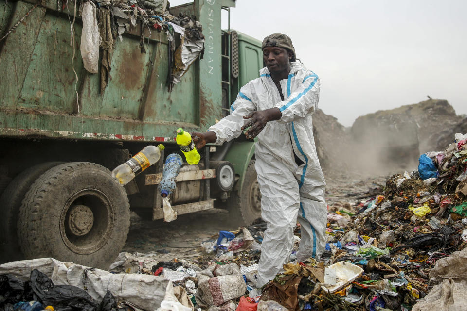 Duncan Wanjohi, scavenges recyclable materials for a living at a garbage dump at Dandora, the largest garbage dump in the Kenyan capital of Nairobi, Sunday, March 28, 2021. He wears a protective medical suit he found in the trash. He and other scavengers, who are not eligible for the COVID-19 vaccine, say the gear protects them from the weather during the rainy season. (AP Photo/Brian Inganga)
