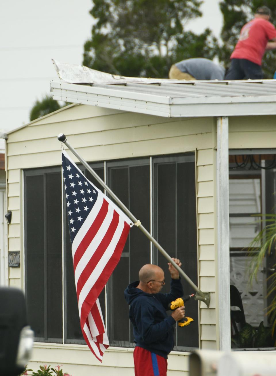 A man uses a drill to repair a damaged flagpole Monday morning at a River Grove Mobile Home Village home.