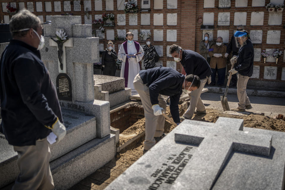 A priest and relatives pray as a victim of the COVID-19 is buried by undertakers at the Almudena cemetery in Madrid, Spain, March 28, 2020. (AP Photo/Olmo Calvo)