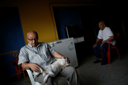 David Riveros, 62, a retired bus driver, pets his dog next to his father-in-law while they rest at home, on the 1st floor of an apartment block in downtown Caracas, Venezuela, March 19, 2019. Riveros, 62, said, "I ran out of water, today I finished all that I had stored". REUTERS/Carlos Garcia Rawlins