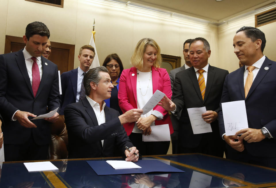 California Gov. Gavin Newsom, seated hands Assemblyman Phil Ting, D-San Francisco, second from right, a copy of his bill that Newsom signed at the Capitol in Sacramento, Calif., Friday, Oct. 11, 2019. The law allows employers, co-workers and teachers to seek gun violence restraining orders for people they believe to be a danger to themselves or others. Ting's measure was one of more than a dozen gun control bills the governor signed Friday. (AP Photo/Rich Pedroncelli)
