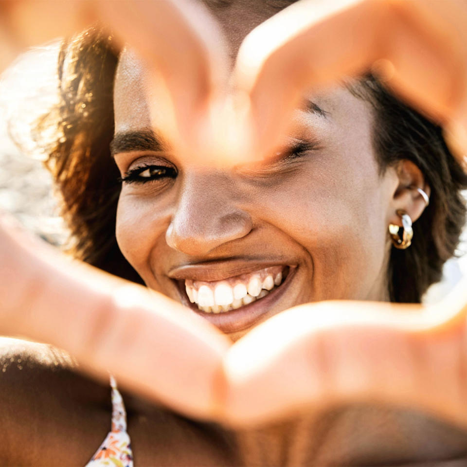 woman in the sun making heart with fingers and smiling