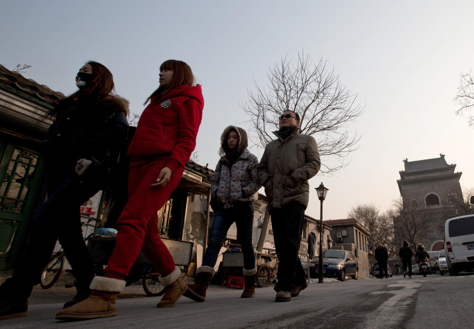 In this photo taken on Dec. 26, 2012, tourists walk past the Hutong houses near the historical Drum and Bell Tower, right in the background, in Beijing. The district government wants to demolish the scuffed courtyard homes, move their occupants to bigger apartments farther from the city center and redevelop a square in 18th century Qing Dynasty fashion. (AP Photo/Andy Wong)