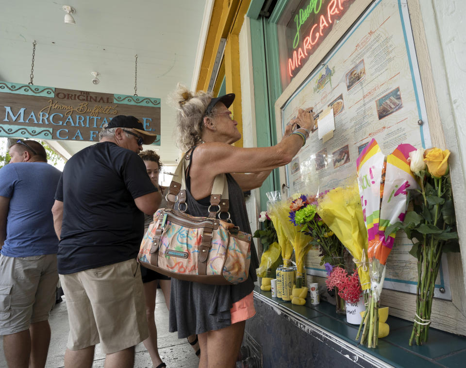 In this photo provided by the Florida Keys News Bureau, Susan Hudnall pins a condolence note about Jimmy Buffett's passing to the front window of the Margaritaville Cafe in Key West, Fla., Saturday, Sept. 2, 2023, in Key West, Fla. Buffett, who popularized beach bum soft rock with the escapist Caribbean-flavored song “Margaritaville” and turned that celebration of loafing into a billion-dollar empire of restaurants, resorts and frozen concoctions, died Friday, Sept 1. He was 76. Hudnall, a visitor from Urbanna, Va, said she had seen every Buffett show in the past 20 years within a 100-mile radius of her home. (Rob O'Neal/Florida Keys News Bureau via AP)