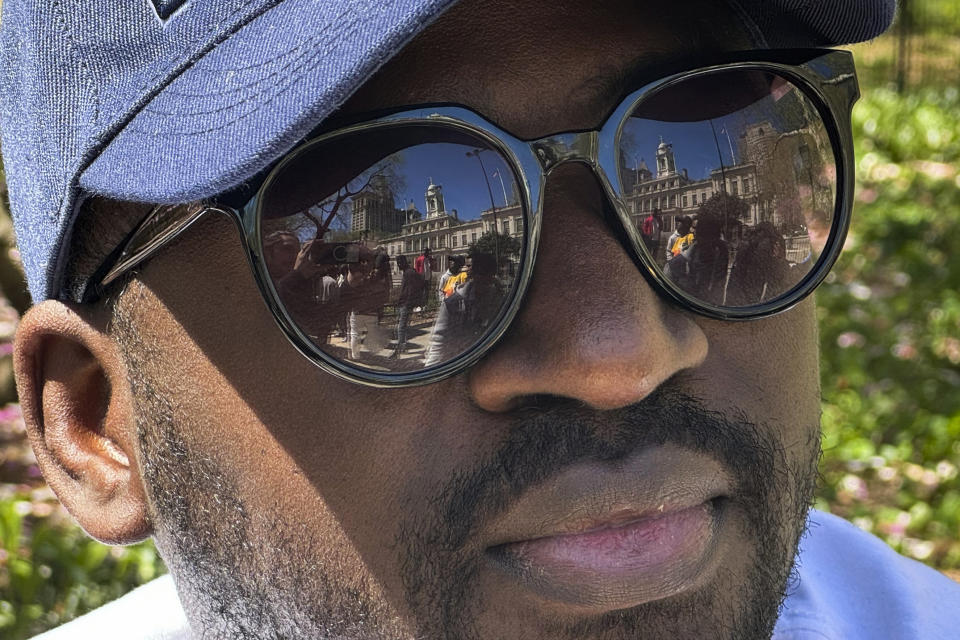 Guinean Diogo Diallo poses for a photo as City hall is reflected in his sunglasses in New York on Tuesday, April 16, 2024. Over 1,500 Black immigrants turned out across from City Hall during a hearing about racial inequities in the city's shelter and immigrant support systems. (AP Photo/Cedar Attanasio)