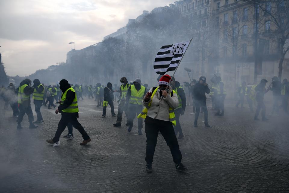 A man holds a Brittany flag as “Yellow vests” (gilets jaunes) protestors clash with riot police amid tear gas on the Champs Elysees in Paris on Dec. 8, 2018 during a protest of against rising costs of living they blame on high taxes. (Photo: Eric Feferberg/AFP/Getty Images)