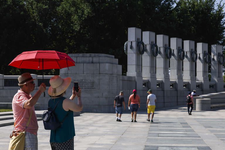 Los turistas usan un paraguas para protegerse del sol mientras visitan el Monumento a la Segunda Guerra Mundial en Washington, DC