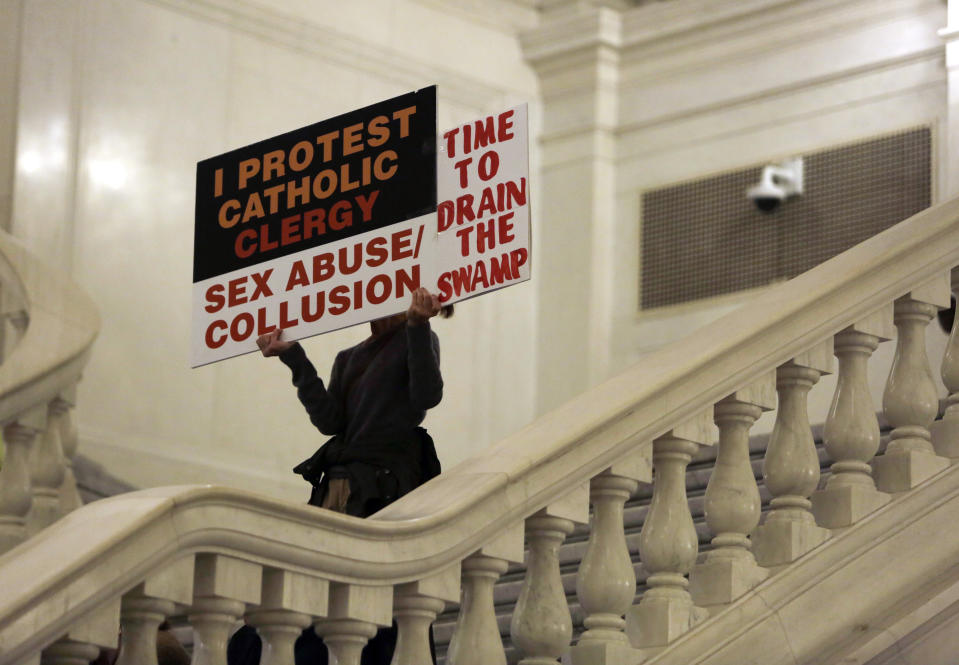 FILE - In this Wednesday Oct. 24, 2018 file photo, a demonstrator holds up protest signs at the Capitol in Harrisburg, Pa. as over 100 people held a rally at the state Capitol Wednesday following the Senate's GOP majority's decision the previous week to leave Harrisburg without voting on a bill that would give victims a two-year window to file lawsuits that would otherwise be outdated. As U.S. Catholic bishops gather for an important national assembly, the clergy sex abuse crisis dominates their agenda. But it's only one of several daunting challenges facing the nation's largest religious denomination. While federal and state law enforcement agencies widen their investigations of abuse, the church finds itself with ever fewer priests and nuns in service. (AP Photo/Jacqueline Larma)