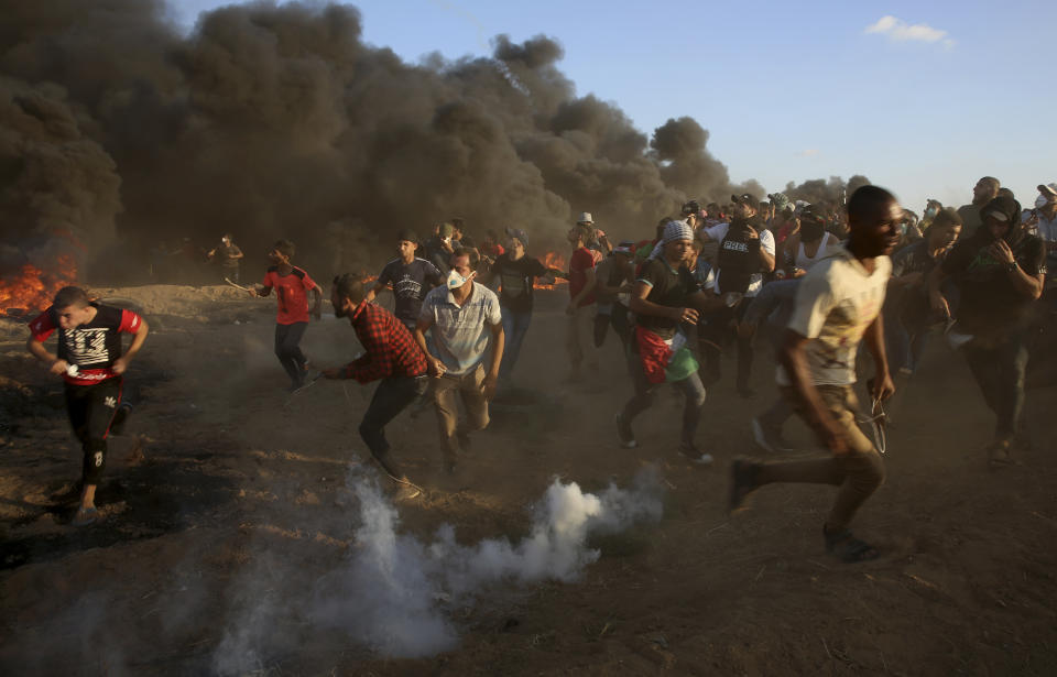 Protesters run to cover from teargas fired by Israeli troops, while others burn tires near fence of Gaza Strip border with Israel during a protest east of Gaza City, Friday, Sept. 14, 2018. Gaza health officials say 3 Palestinians, including 12-year-old boy, were killed by Israeli army fire in protests along Gaza's perimeter fence. (AP Photo/Adel Hana)