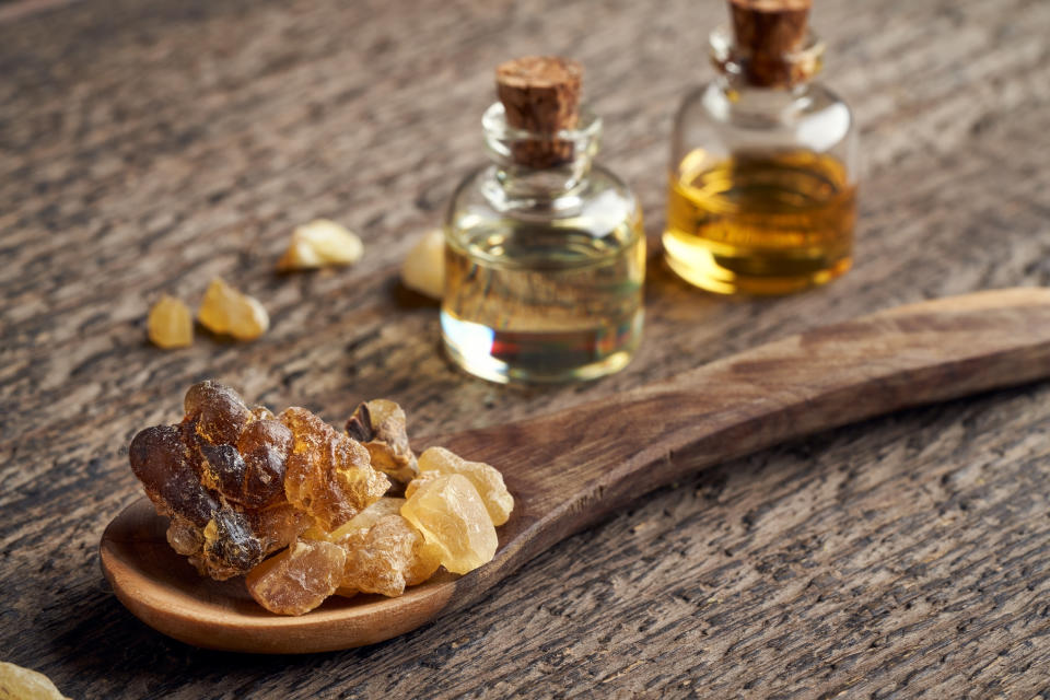 Frankincense resin crystals on a spoon, with essential oil bottles in the background