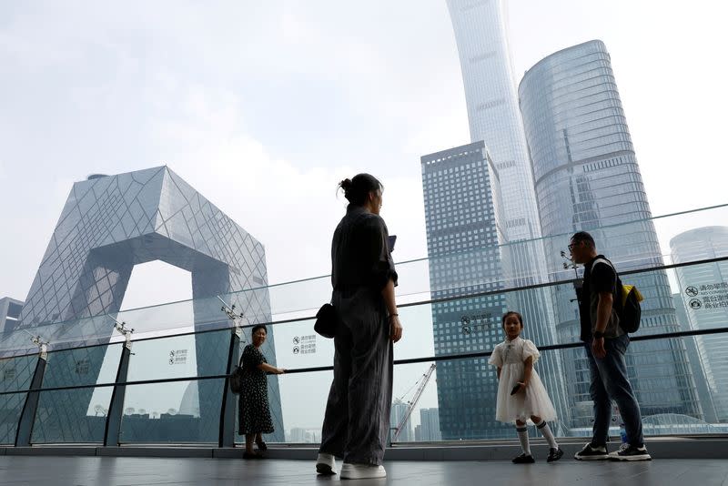 FILE PHOTO: People stand at a shopping mall near the CCTV headquarters and China Zun skyscraper, in Beijing's central business district (CBD)