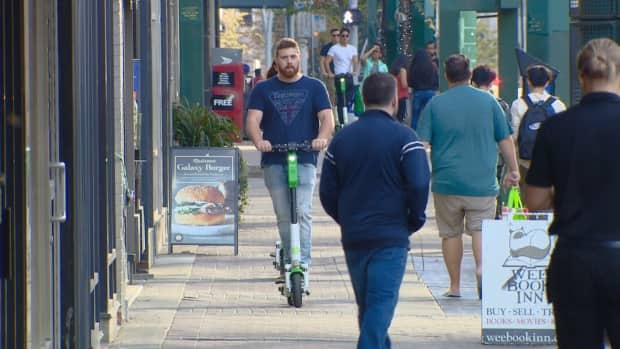 An e-scooter rider cruises down the sidewalk on a busy weekend day in Edmonton.