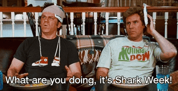 John C. Reilly and Will Ferrell sit on a couch, both appearing frustrated. The text reads, "What are you doing, it's Shark Week!"
