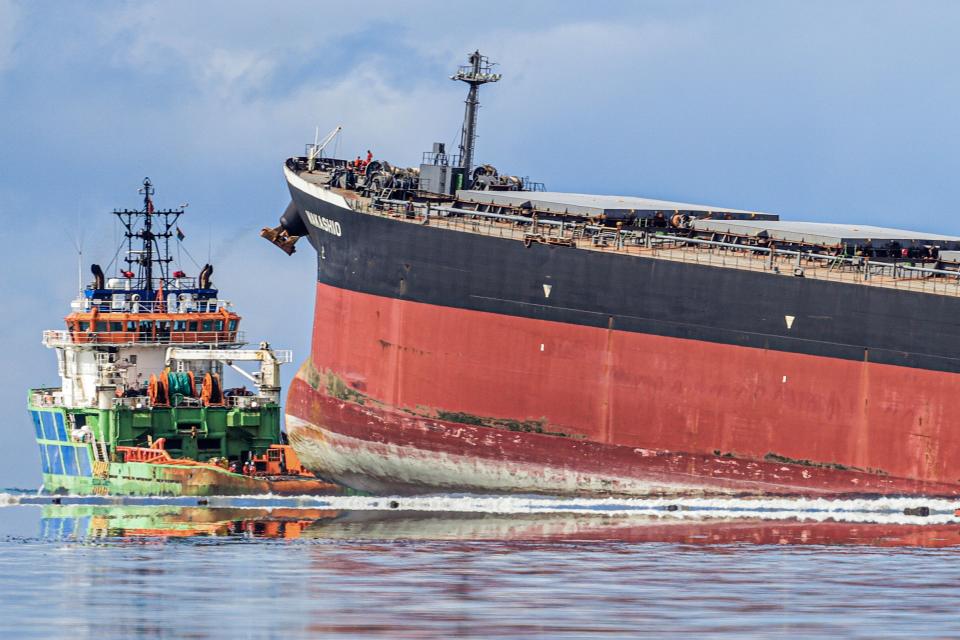 A smaller ship runs alongside the MV Wakashio that has ran aground off Mauritius.