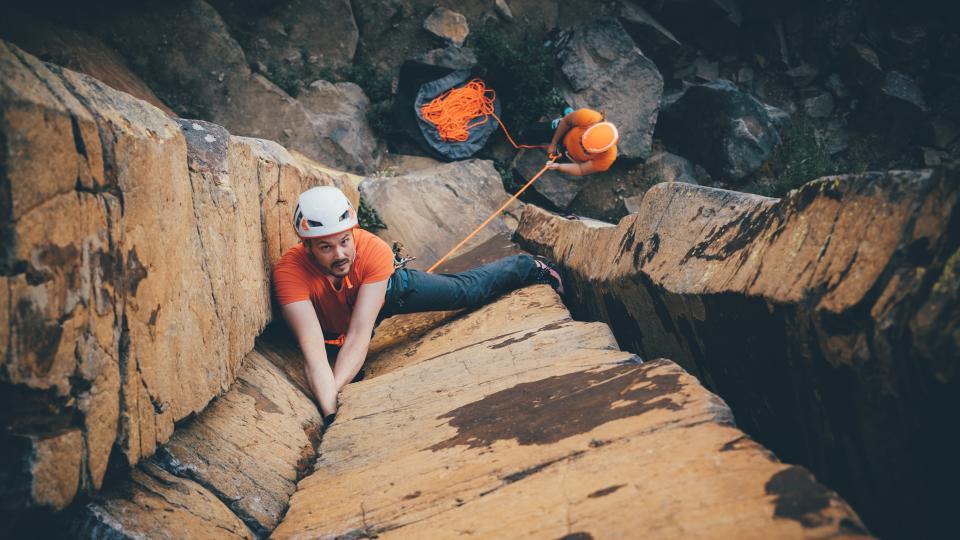 Rock climber looking up at the camera while climbing a dramatic basalt column near Vernon, BC