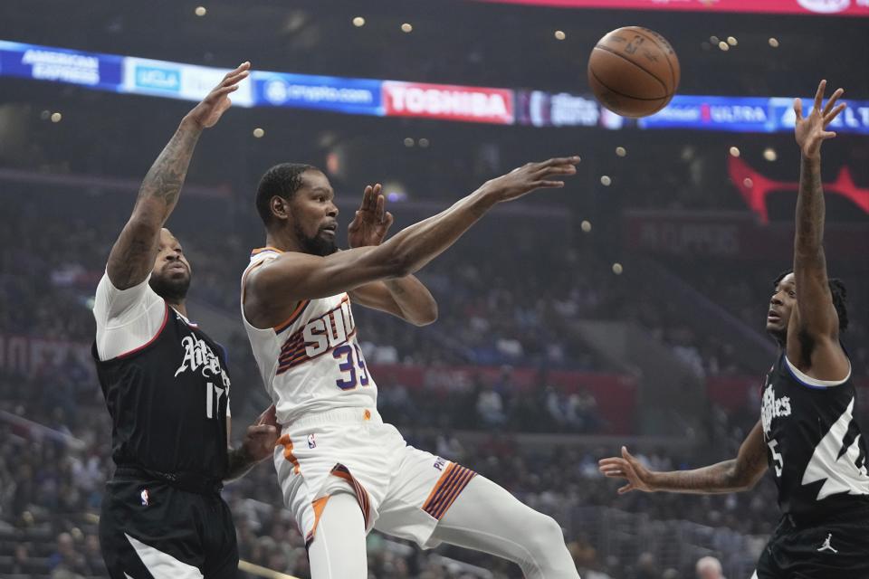 Phoenix Suns forward Kevin Durant, center, passes the ball while under pressure from Los Angeles Clippers forward P.J. Tucker, left, and guard Bones Hyland during the first half of an NBA basketball game Wednesday, April 10, 2024, in Los Angeles. (AP Photo/Mark J. Terrill)