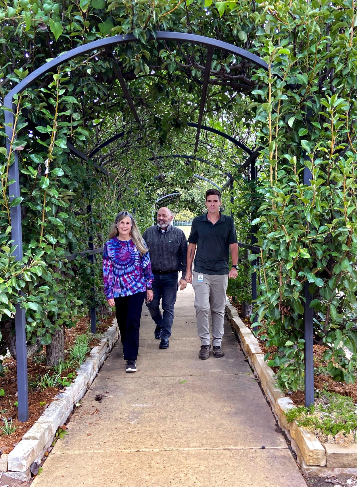 Jordan Davis, Pam Patty and Steve Petty walk under a trellis at the Lynn Institute Community Garden at Chesapeake, NW 62 and N Shartel Ave.