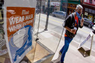 John Bechtold puts his face covering on as he passes his storefront sign that lists COVID-19 protective covering required to enter in his retail shop, Friday, May 14, 2021, in Pittsburgh's South Side neighborhood. (AP Photo/Keith Srakocic)