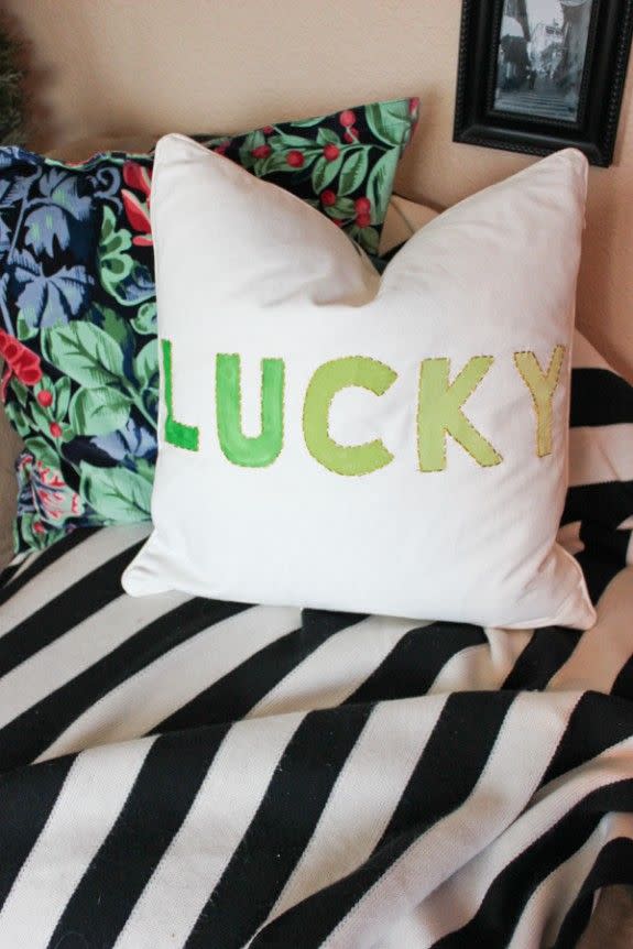 white pillow with lucky painted and stitched across it sitting on a coach