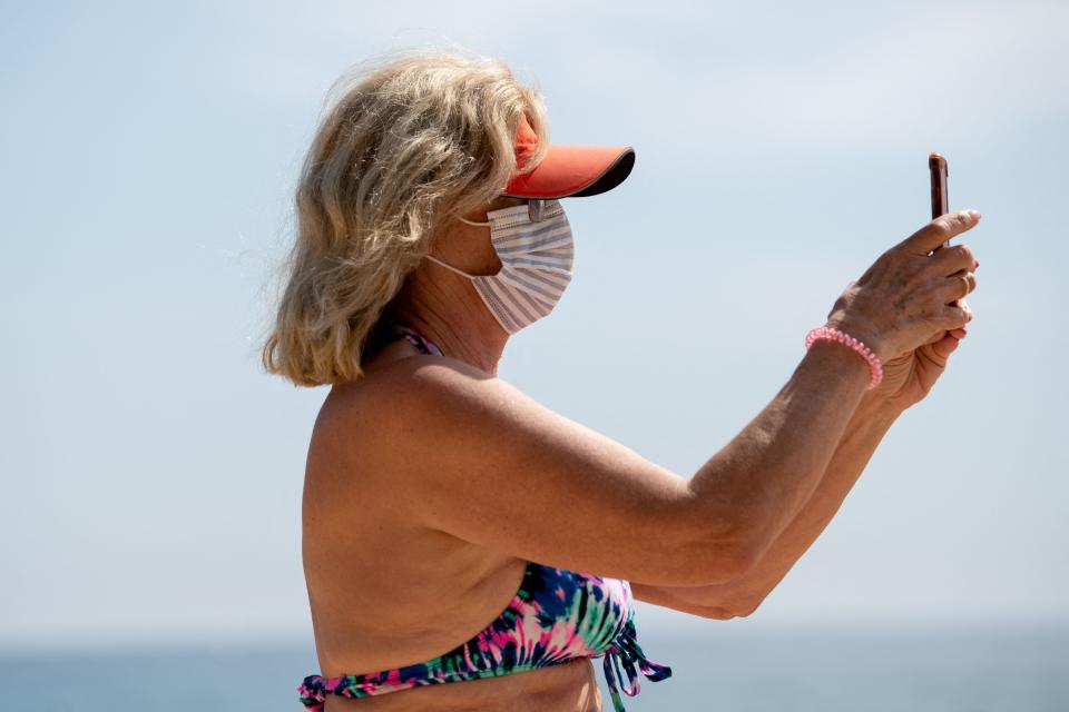 A woman wearing a face mask uses her smartphone on Sa Conca Beach in Castell-Platja D'Aro near to Girona, Spain, on March 31, 2021.