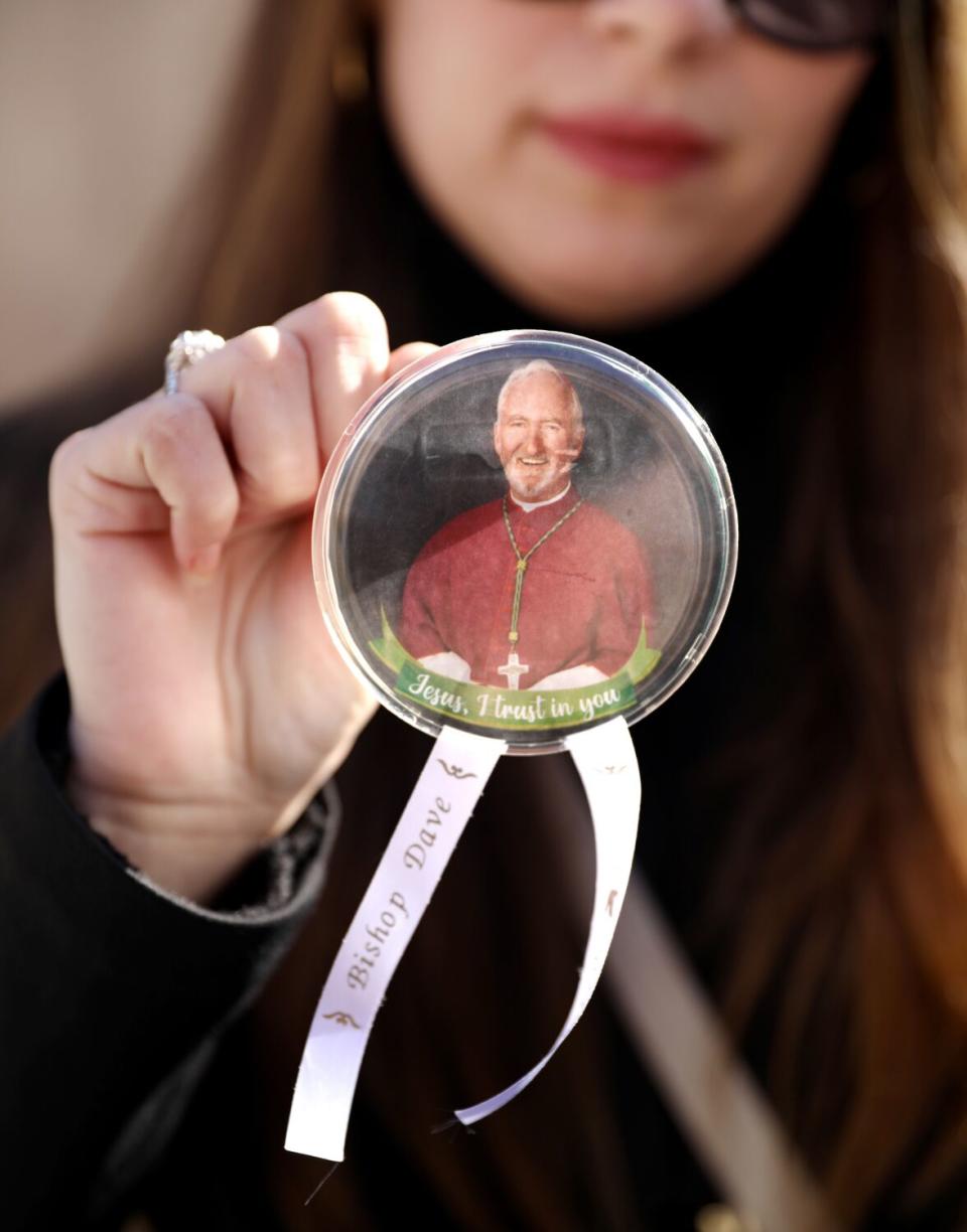 A woman holds up a button with a picture of Bishop O'Connell