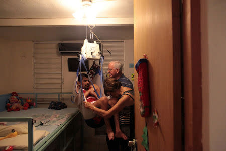 Ramona Febo-Boarman kisses her son Joey's knee as she and her husband Jim move Joey into bed with the help of portable overhead lift at their home in Bayamon, Puerto Rico, December 1, 2016. REUTERS/Alvin Baez