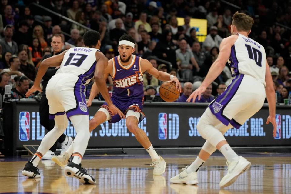 Phoenix Suns guard Devin Booker (1) drives between Sacramento Kings forward Keegan Murray (13) and center Domantas Sabonis (10) in the first half Tuesday, Feb. 13, 2024, at Footprint Center in Phoenix, Arizona. Rick Scuteri/USA TODAY Sports