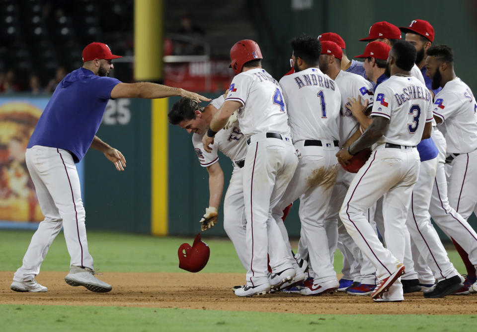 Texas Rangers' Nomar Mazara, left, and teammates mob Nick Solak, second from left dropping his helmet, after Solak reached first on a fielding error by Los Angeles Angels' Albert Pujols that allowed Delino DeShields to score in the 11th inning of a baseball game in Arlington, Texas, Tuesday, Aug. 20, 2019. The Rangers won 3-2. (AP Photo/Tony Gutierrez)