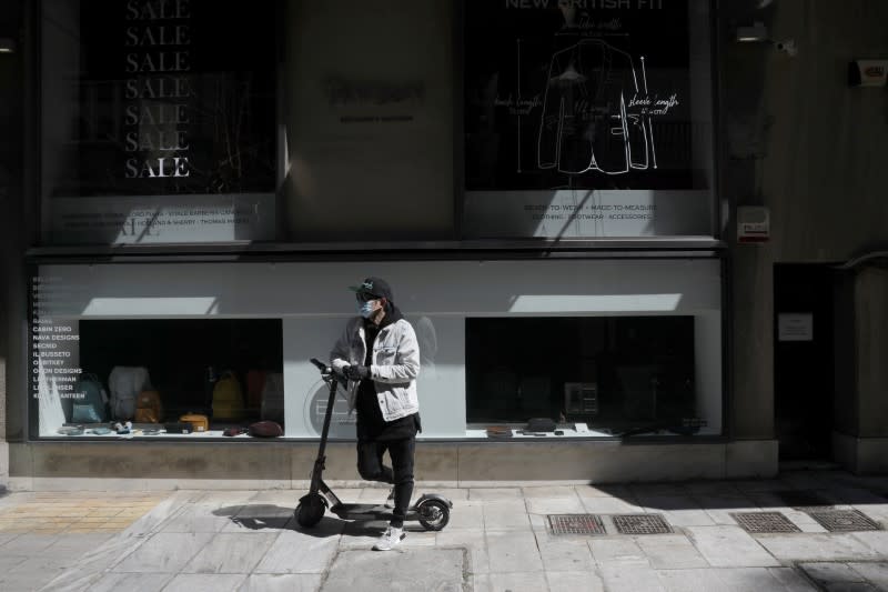 A man wears a protective face mask as he stands on his scooter outside a closed store, as a precaution against the spread of the coronavirus disease (COVID-19), in Athens
