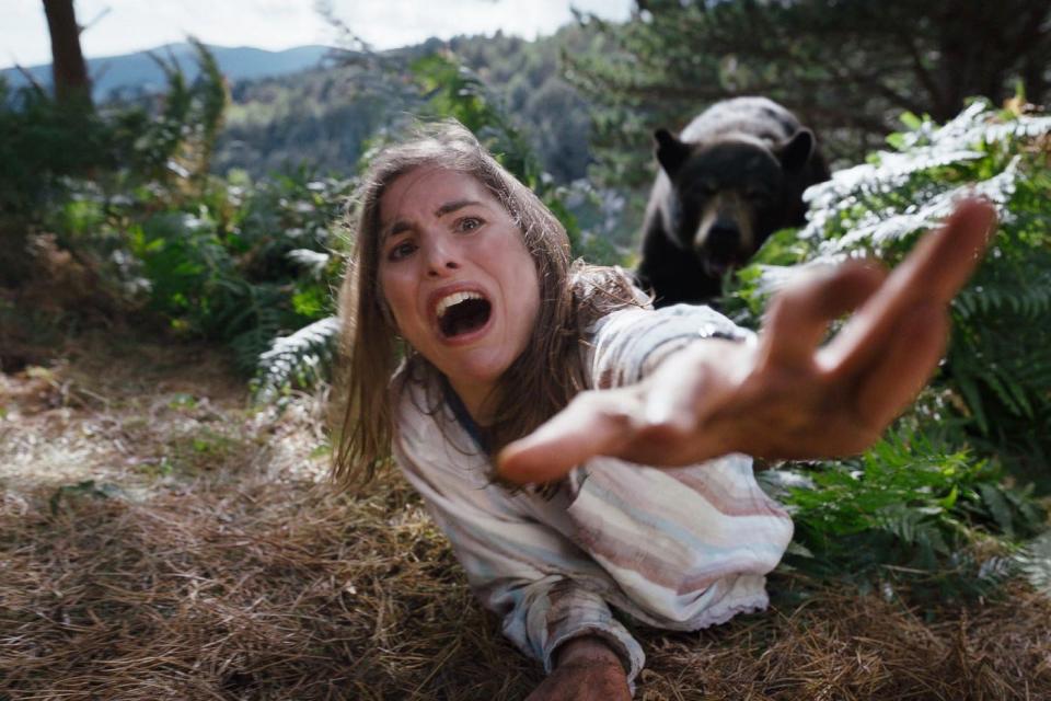 A woman stretching out her hand as a bear pulls her into the woods