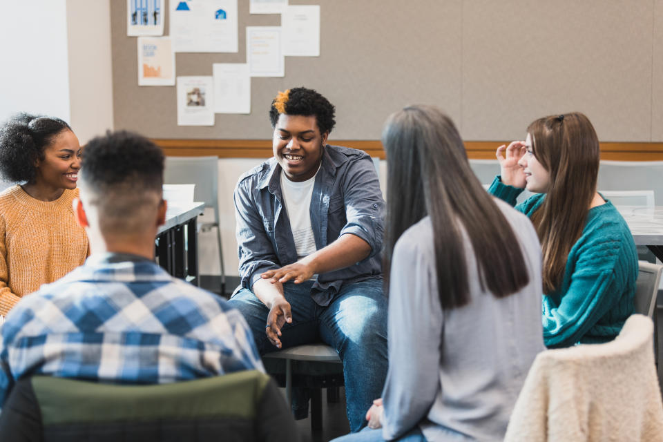 A group of teenagers sit in chairs in a circle during a discussion at a support group