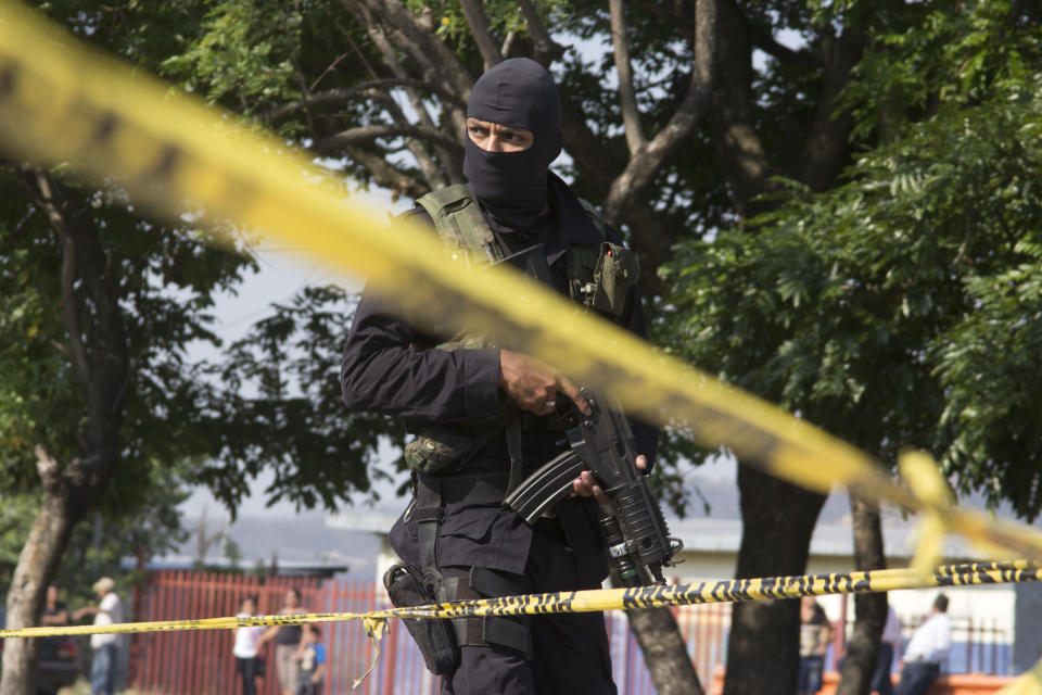 In this April 13, 2014 photo, a police officer guards the scene after gunmen using assault weapons opened fire, killing four men in Santiago Texacuangos, 20 kms. south of San Salvador, El Salvador. Public Safety Minister Ricardo Perdomo said the country’s Mara Salvatrucha and Mara 18 street gangs are buying automatic rifles in the black market in Honduras and Guatemala, and also getting them from the brutal Zetas drug cartel. (AP Photo/Salvador Melendez)