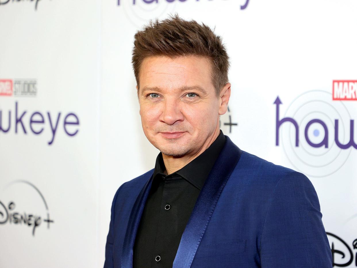 Jeremy Renner poses for photos on the red carpet in a black shirt and dark blue suit jacket.