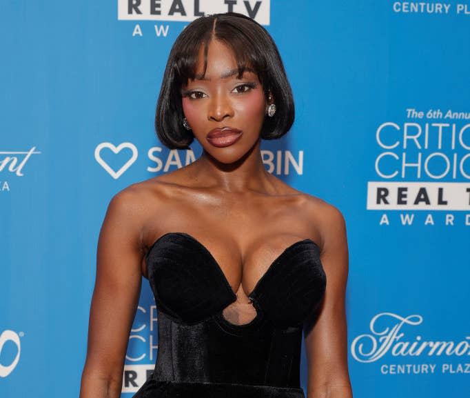 A woman poses on a blue carpet at the Critics Choice Real TV Awards wearing a strapless velvet dress with a sweetheart neckline