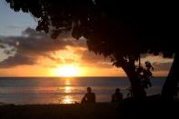 FILE PHOTO: Surfers watch the sun set after surfing along the coast of Kiritimati Island, part of the Pacific Island nation of Kiribati