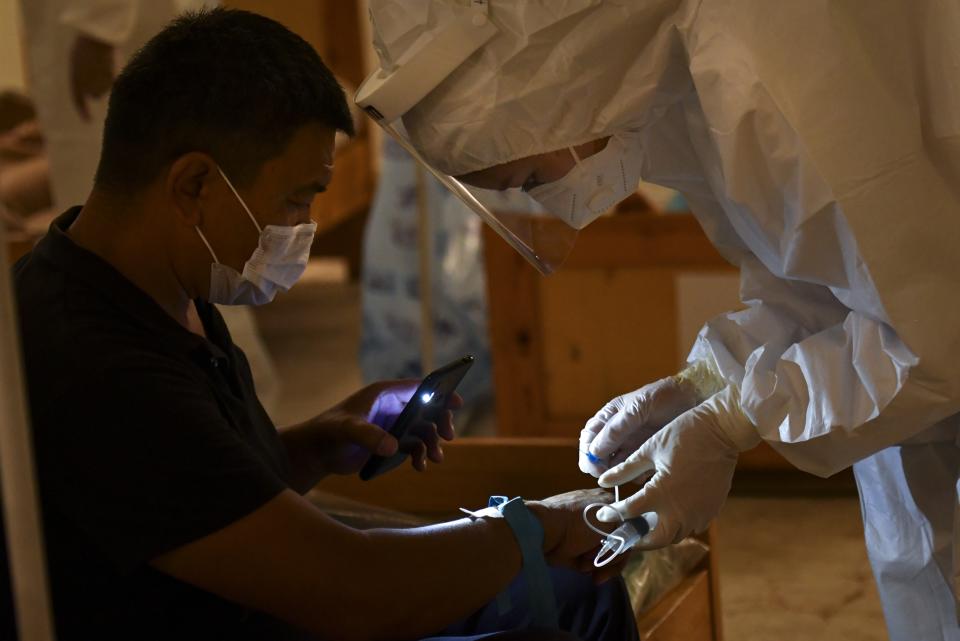 A medical worker places an intravenous drip for a patient who is suspected of having the coronavirus as he lights an area with his phone in a restaurant converted to a clinic in Bishkek, Kyrgyzstan, Wednesday, July 22, 2020. The restaurant is being used as night-time clinic to support the country's health care system, struggling with the coronavirus outbreak. Doctors and nurses from other facilities work there and treat people between 8 p.m. and 8 a.m. (AP Photo/Vladimir Voronin)