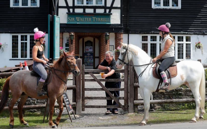 On the hoof: New Forest pub landlord Nick Cross offers a takeaway pint of cider to Georgia Prendergast and Chloe Hughes and their horses Snowy and Whiteheart - BNPS