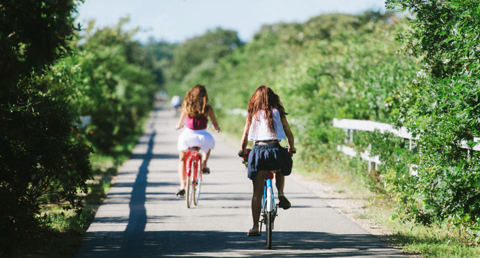 two girls riding bicycles on path surrounded by trees