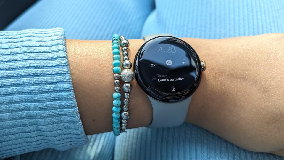 Google Pixel Watch worn on a wrist with beaded bracelets.