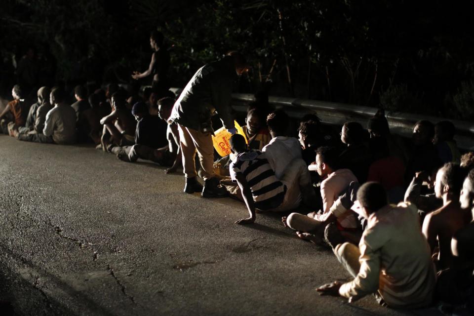 Migrants sit on the ground after storming a fence to enter the Spanish enclave of Ceuta, Spain, Friday, Feb. 17, 2017. An emergency team in Ceuta is assisting more than 300 migrants who crossed the fence surrounding Spain's enclave in North Africa early Friday, a spokesman for the local Red Cross said. Spain's Civil Guard said that a surveillance camera registered how more than 500 people approached the fence with tools and clubs that they used for breaking one of the gates. (AP Photo/Jesus Moron)