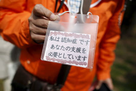 61-year-old Masahiko Sato, who has become a kind of "poster boy" for Japan's growing number of people with dementia, shows a card reading "I have dementia. I need your assistance" as he strolls during a cherry blossom viewing event at Omiya park in Omiya, north of Tokyo, Japan, March 27, 2016. REUTERS/Issei Kato