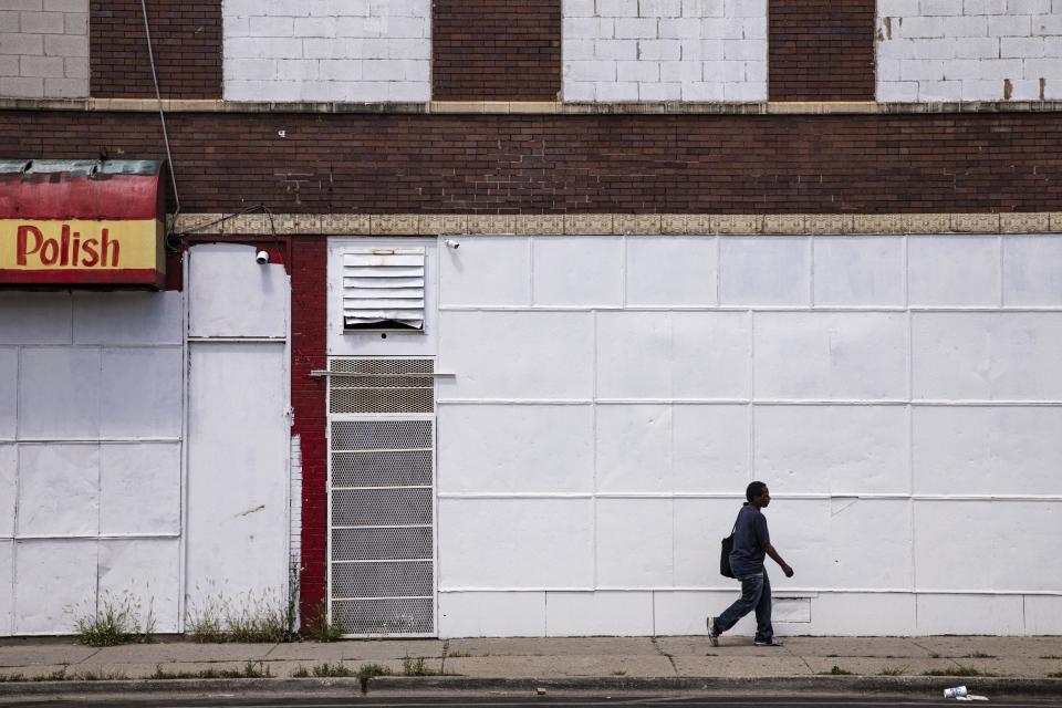 In this Friday, Aug. 9, 2019, photo, a man walks on a sidewalk past boarded up business in Chicago's Englewood neighborhood. As of 2015, roughly 22% of Atlanta's population was living in a low-income community more than a mile from a food store, and in Chicago, that number is 5%, according to the U.S. Department of Agriculture. (AP Photo/Amr Alfiky)