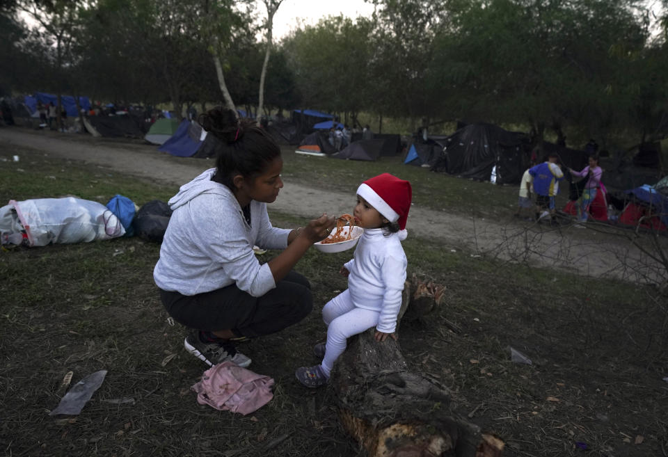 A Venezuelan migrant feeds her daughter at a makeshift camp set up along a river bank, in Matamoros, Mexico, Thursday, Dec. 22, 2022. (AP Photo/Fernando Llano)