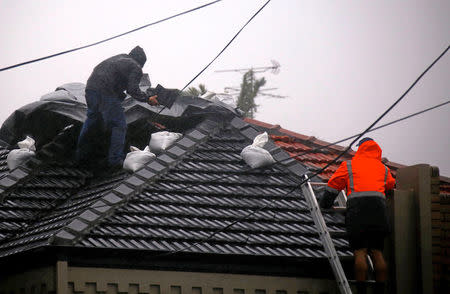 Two men work on covering a damaged roof on a house in severe weather bringing strong winds and heavy rain hits the eastern coast of Australia near Coogee Beach in Sydney, June 5, 2016. REUTERS/David Gray